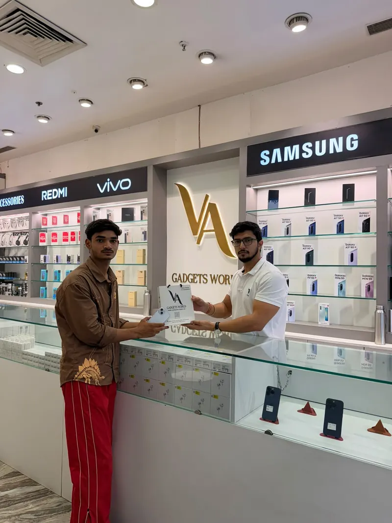 A customer at VA Gadgets World receiving his new phone and a branded VA shopping bag from the staff at the counter.
